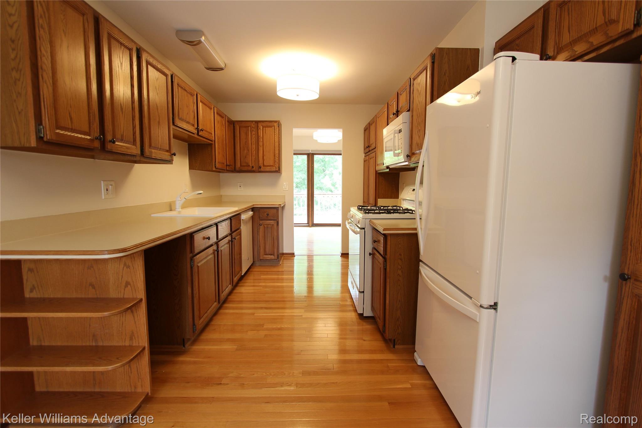 21850 River Ridge Trail Farmington, MI 48335 - Photo 14 of 33 Galley kitchen featuring wood-finish flooring, abundant wood cabinetry, integrated white appliances, and a double basin sink