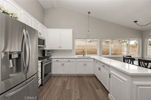 a large kitchen with a stove a sink dishwasher a refrigerator and white cabinets with wooden floor