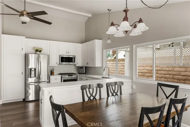 a kitchen with stainless steel appliances granite countertop a dining table chairs refrigerator and microwave