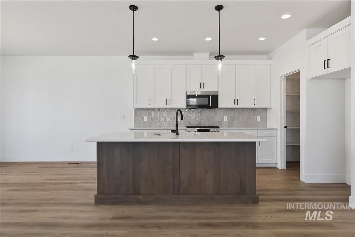 776 South Calhoun Lane Star, ID 83669 - Photo 6 of 49 Open-concept kitchen featuring a dark wood-finish island with a light-toned countertop, white cabinetry with black hardware, a grey subway tile backsplash, and recessed lighting