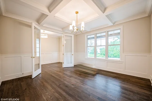 an empty room with wooden floor chandelier and windows
