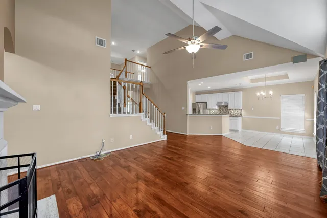 a view of an empty room and kitchen view with wooden floor