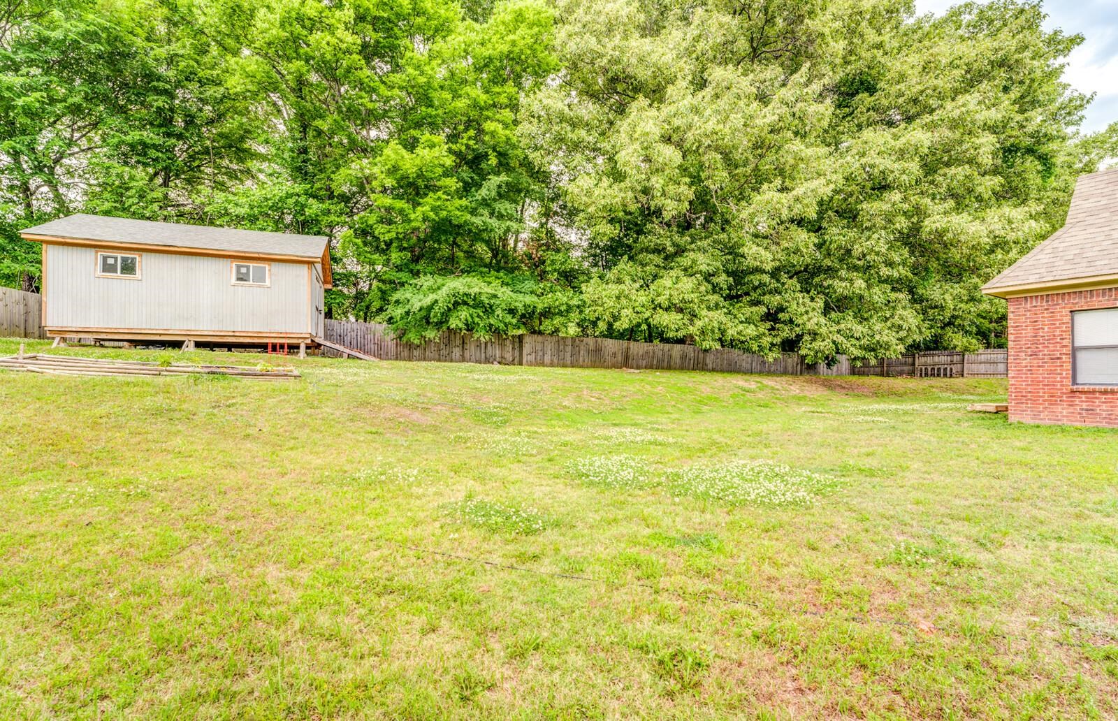 4671 Hampton Ridge Lane Bartlett, TN 38002 - Photo 34 of 40 Spacious lawn area featuring a detached storage shed with dual windows and a gabled roof, alongside a wood privacy fence and mature trees