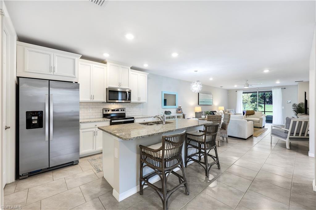 14551 Edgewater Circle Naples, FL 34114 - Photo 11 of 26 Kitchen featuring appliances with stainless steel finishes, light tile patterned flooring, light stone countertops, a breakfast bar area, and decorative backsplash