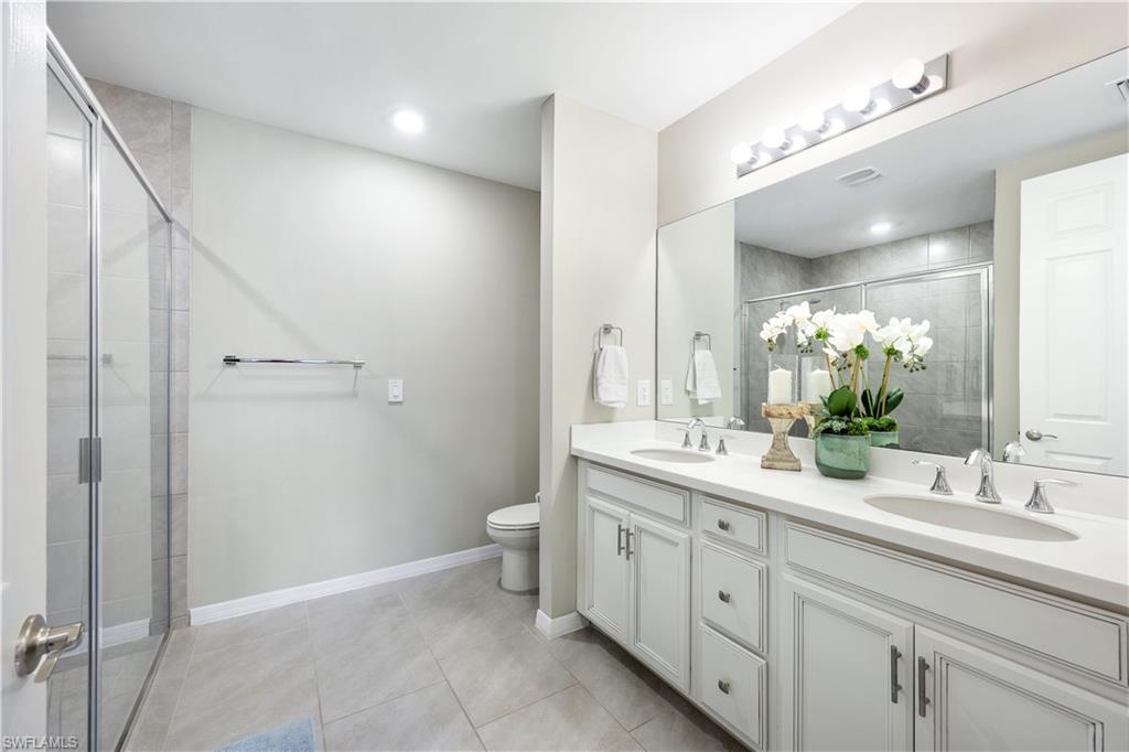 14551 Edgewater Circle Naples, FL 34114 - Photo 14 of 26 Bathroom with double vanity, light tile patterned floors, and a shower stall