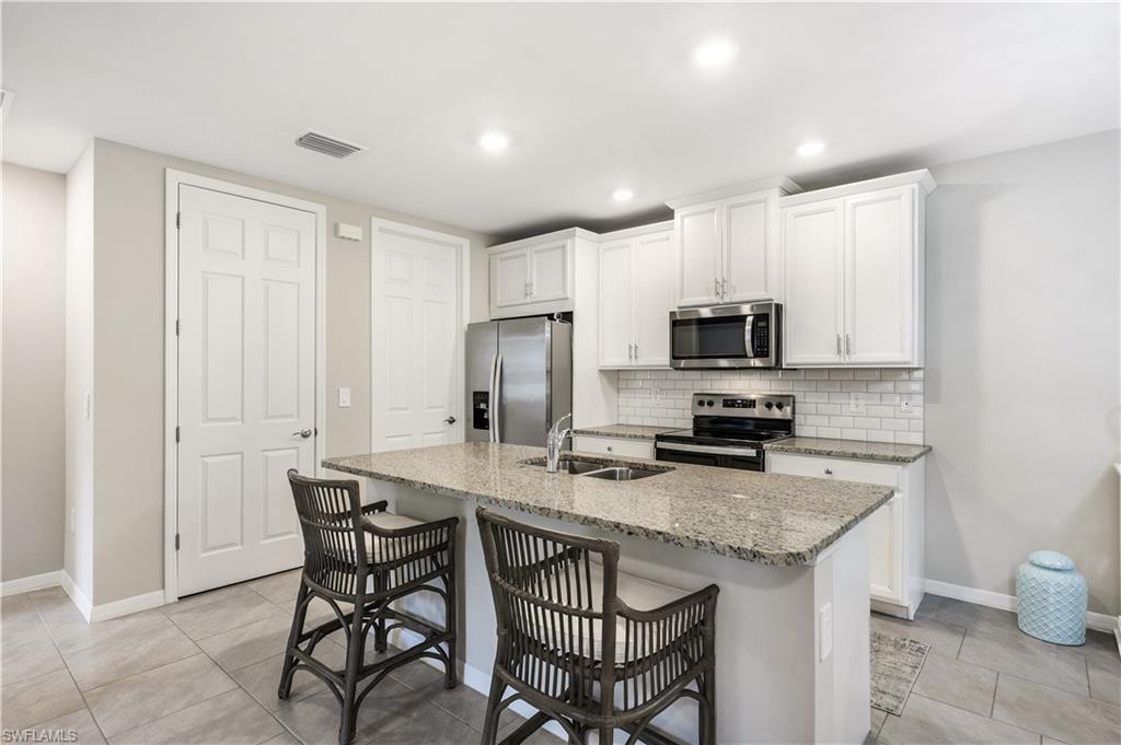 14551 Edgewater Circle Naples, FL 34114 - Photo 9 of 26 Kitchen featuring light stone counters, stainless steel appliances, white cabinetry, a breakfast bar area, and tasteful backsplash