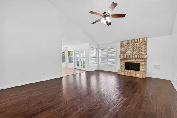 a view of an empty room with wooden floor a ceiling fan and a window
