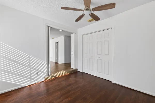an empty room with wooden floor chandelier fan and windows