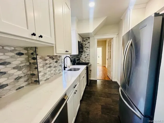 a kitchen with stainless steel appliances a refrigerator a sink and white cabinets