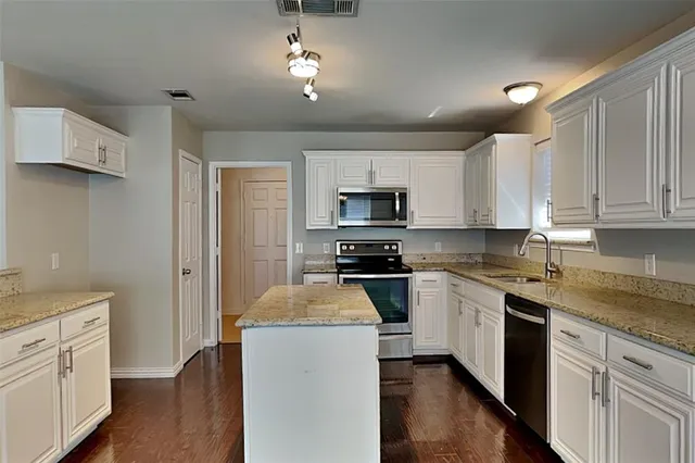 a kitchen with granite countertop a sink stainless steel appliances and white cabinets