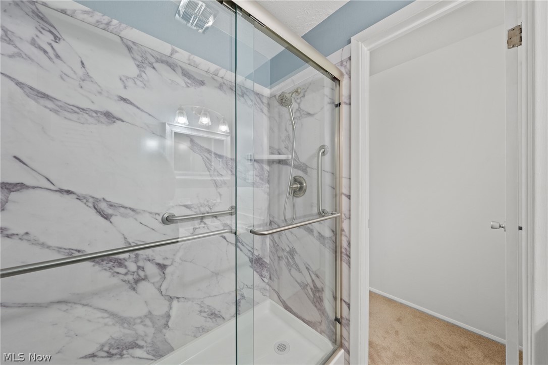 3070 Kent Road, Unit 312D Stow, OH 44224 - Photo 30 of 49 Spa-inspired primary bathroom showcasing a frameless glass shower enclosure with elegant veined marble tile surround, dual chrome fixtures, and brushed nickel grab bars