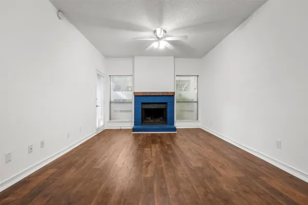 a view of an empty room with wooden floor fireplace and a window