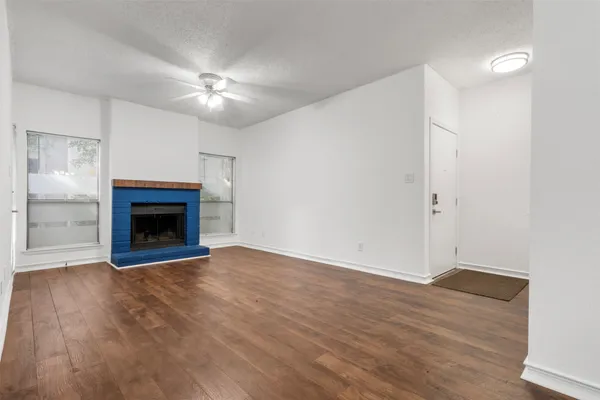 a view of an empty room with wooden floor fireplace and a window