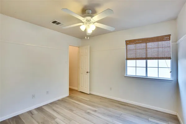 an empty room with wooden floor fan and windows