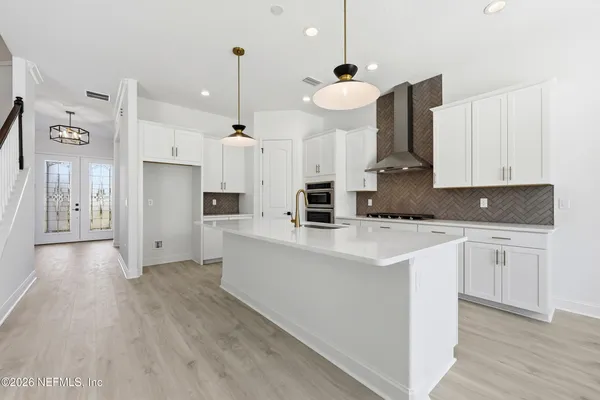 a kitchen with stainless steel appliances a stove a sink a refrigerator and white cabinets with wooden floor