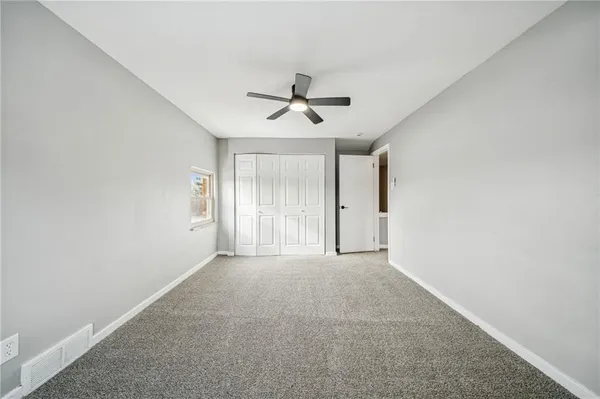 an empty room with chandelier fan and windows