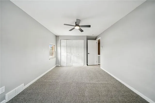 an empty room with chandelier fan and windows
