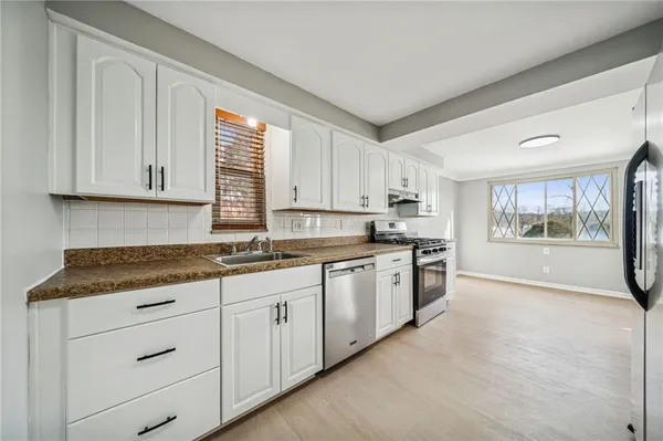 a kitchen with granite countertop a stove a sink and white cabinets