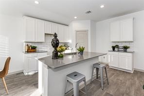 7811 Golden Rubia Lane Rosharon, TX 77583 - Photo 4 of 10 This modern kitchen features white cabinetry, a spacious island with gray countertops, and stylish bar stools. The space is bright with recessed lighting and wood-look flooring, offering a clean and inviting atmosphere.