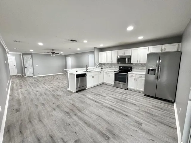 a open kitchen with stainless steel appliances granite countertop a stove top oven a refrigerator and white cabinets with wooden floor