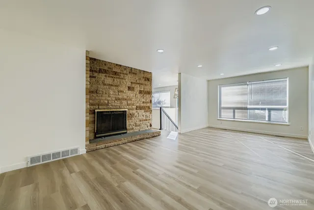 an empty room with wooden floor fireplace and windows
