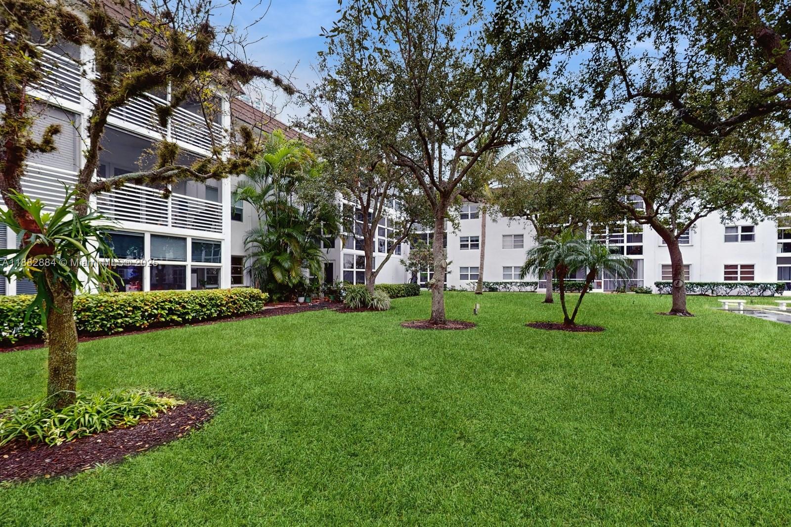 1501 South Ocean Boulevard, Unit 301 Lauderdale-by-the-Sea, FL 33062 - Photo 15 of 17 a view of a white house in front of a big yard with plants and large trees