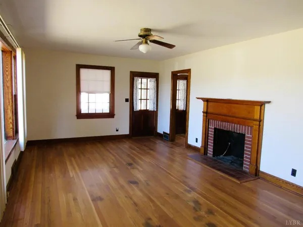 a view of an empty room with wooden floor fireplace and a window
