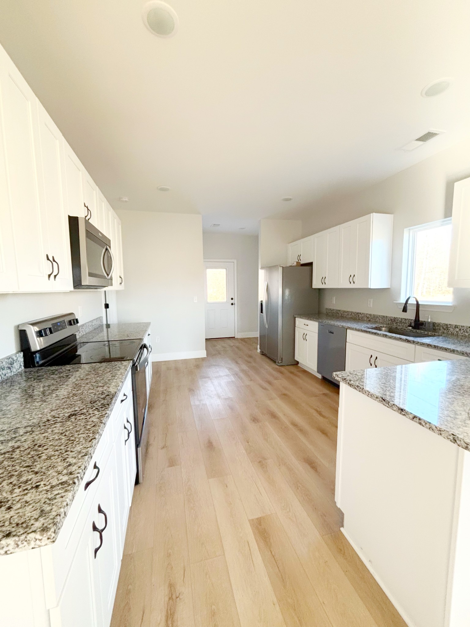 a large kitchen with granite countertop a sink a counter top space and stainless steel appliances