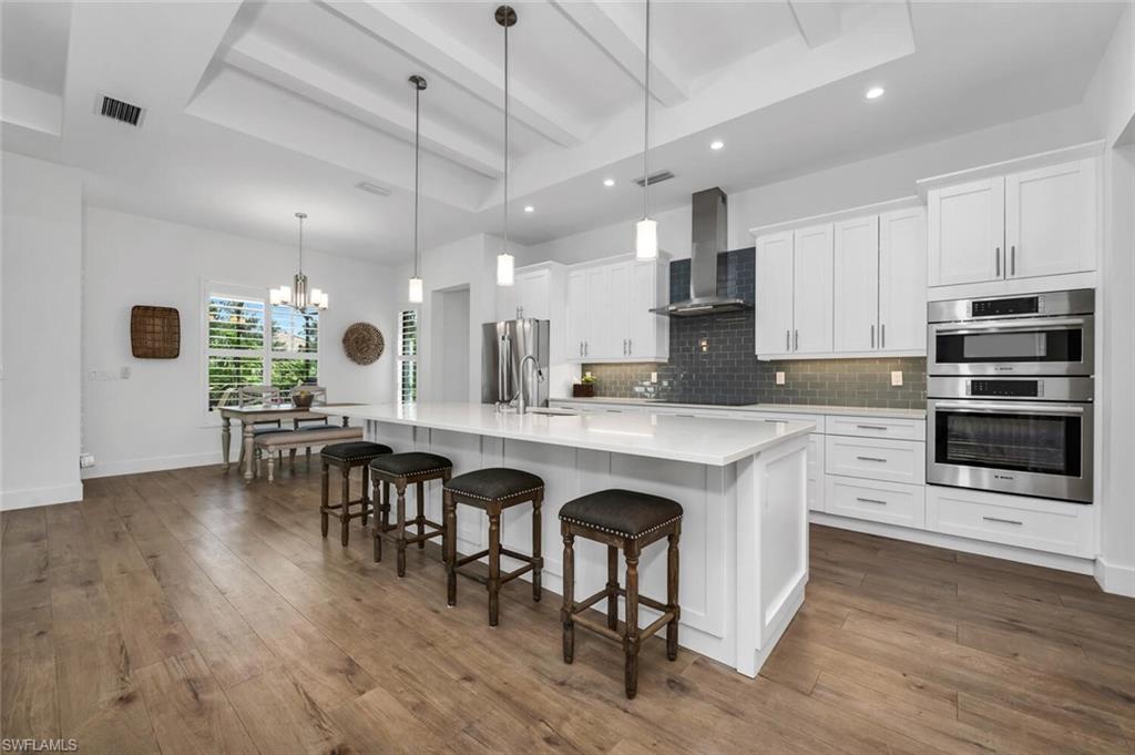 7437 Acorn Way Naples, FL 34119 - Photo 2 of 19 a kitchen with stainless steel appliances granite countertop a stove a refrigerator a sink a dining table and chairs with wooden floor