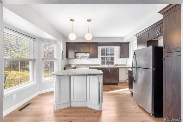 a kitchen with stainless steel appliances granite countertop a refrigerator a sink dishwasher a stove a oven and a dining table with wooden floor