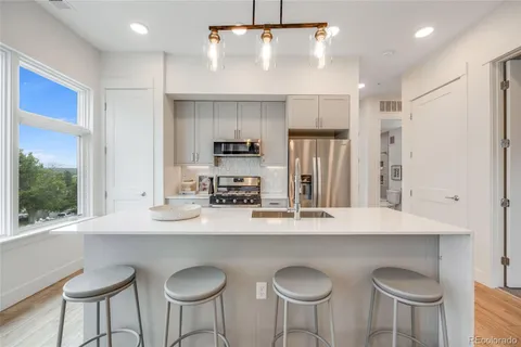 a kitchen with stainless steel appliances granite countertop a sink a stove a refrigerator and white cabinets with wooden floor