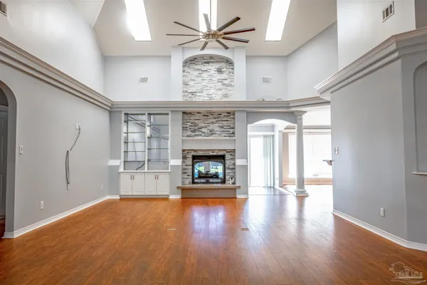 a view of an empty room with chandelier fan and wooden floor