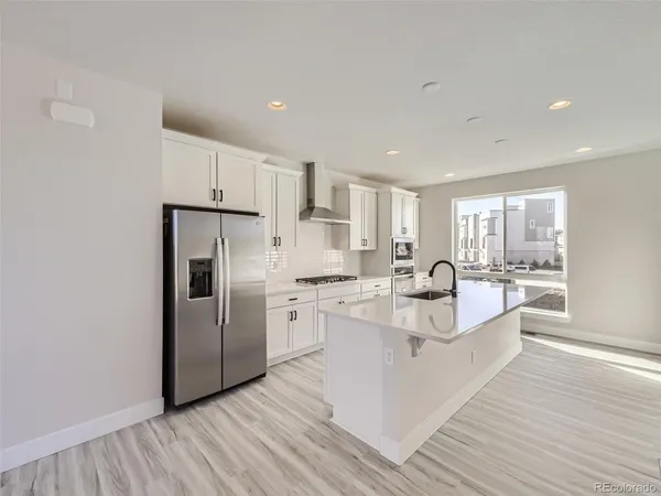 a large white kitchen with a refrigerator a stove top oven and white cabinets