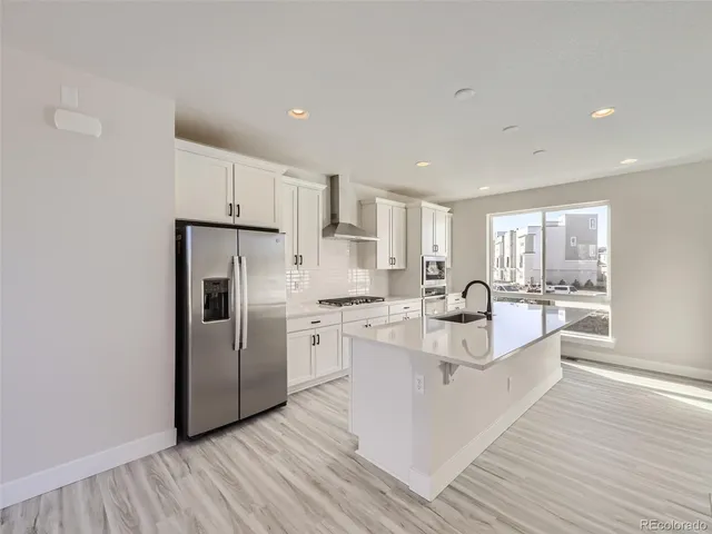 a large white kitchen with a refrigerator a stove top oven and white cabinets