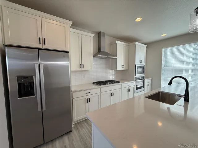 a kitchen with stainless steel appliances granite countertop a refrigerator a sink a stove and white cabinets with wooden floor