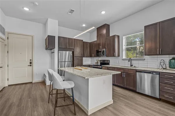 a kitchen with wooden cabinets a sink a stove a refrigerator and island with wooden floor
