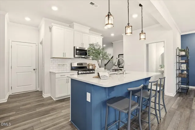 a kitchen with stainless steel appliances granite countertop white cabinets a sink a stove a refrigerator and island with wooden floor