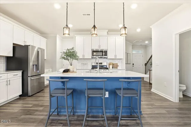 a kitchen with stainless steel appliances kitchen island granite countertop a refrigerator a oven a stove and white cabinets with wooden floor