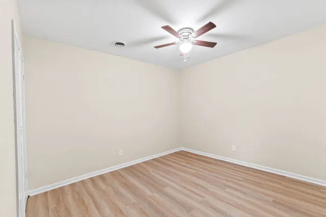 an empty room with wooden floor and fan