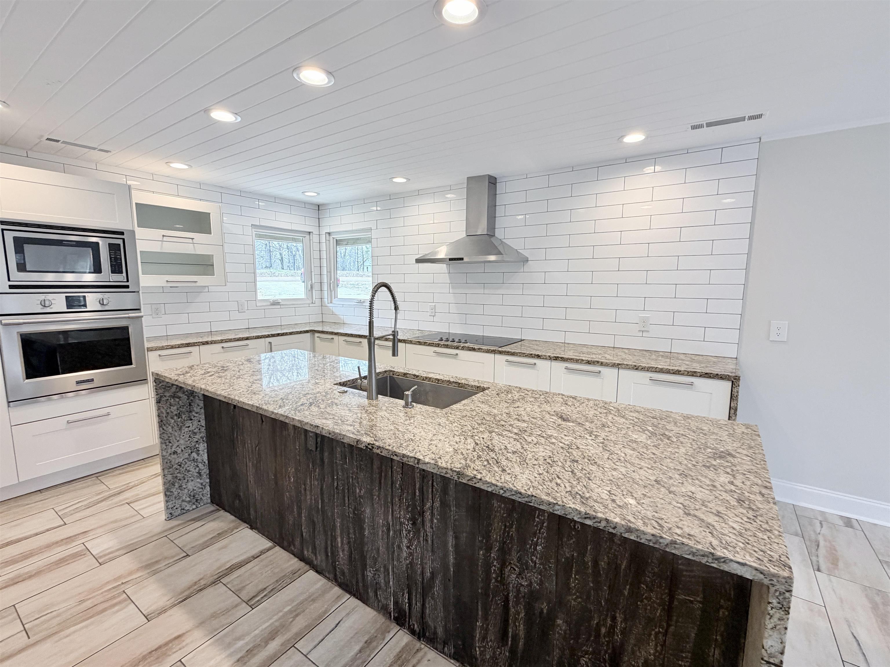 955 Country Club Road Somerville, TN 38068 - Photo 17 of 40 Dual tone kitchen with light stone counters, stainless steel appliances, exhaust hood, wood tiled floors, and a kitchen island with sink