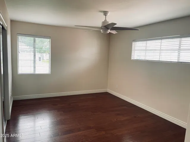 an empty room with wooden floor fan and windows