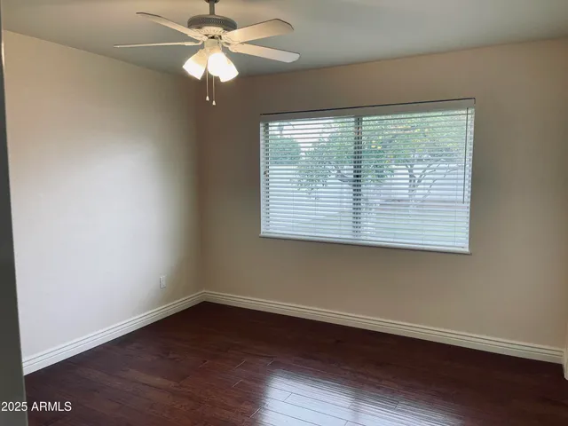 an empty room with wooden floor chandelier fan and windows