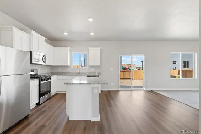 a kitchen with stainless steel appliances granite countertop a refrigerator a stove top oven a sink dishwasher and white cabinets with wooden floor