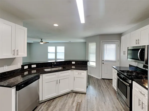 a kitchen with granite countertop a sink a stove cabinets and wooden floor