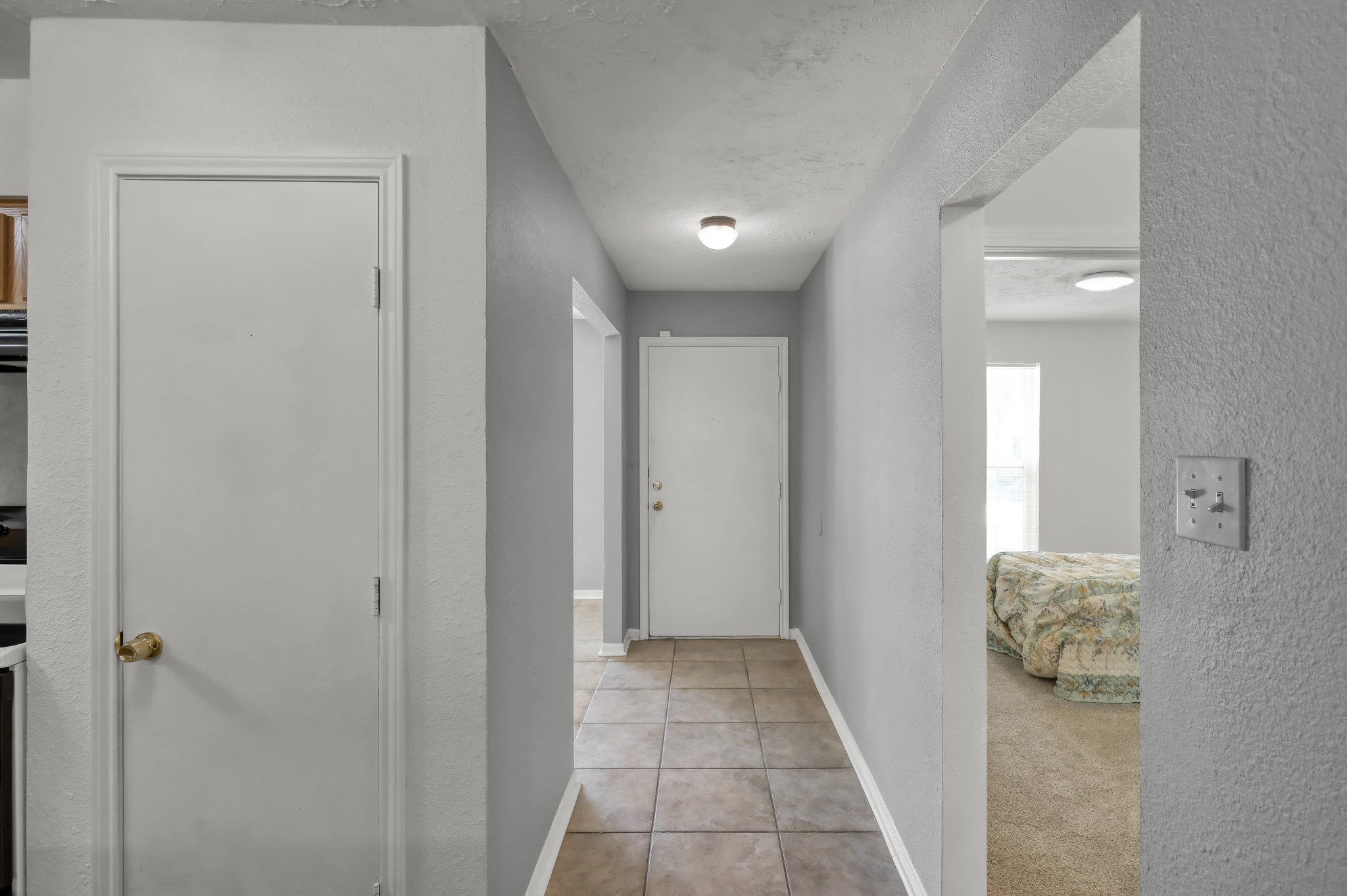 4314 Enchantedgate Drive Spring, TX 77373 - Photo 5 of 47 This photo shows a bright hallway with tiled flooring, neutral walls, and a simple light fixture. There's a kitchen pantry door on the left, an entrance to a carpeted guest bedroom on the right, and the front door at the end of the hall.