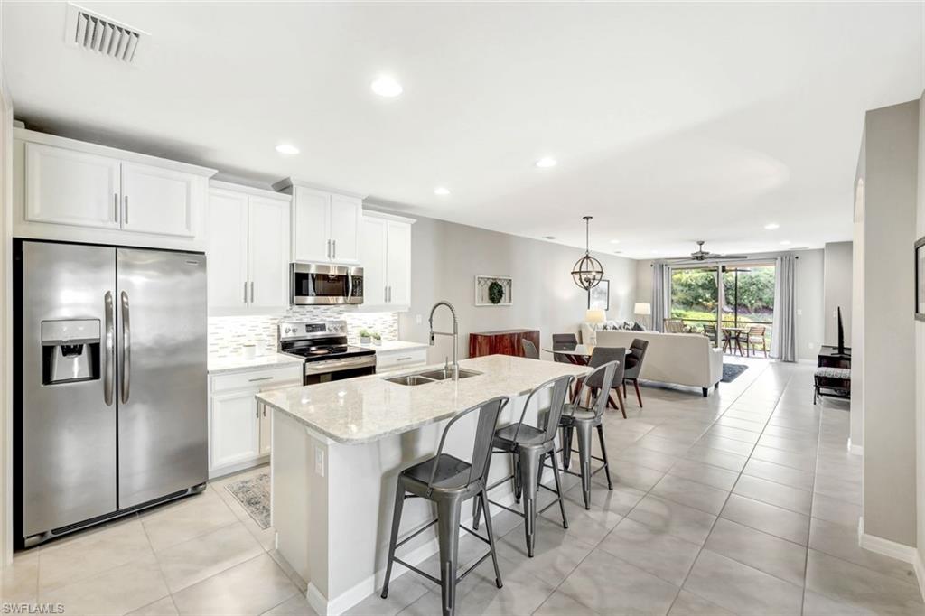 14863 Edgewater Circle Naples, FL 34114 - Photo 4 of 35 a kitchen with stainless steel appliances a dining table chairs stove refrigerator and cabinets