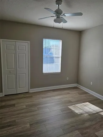 an empty room with wooden floor chandelier fan and windows