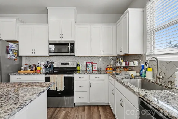 a kitchen with granite countertop a sink dishwasher stove and white cabinets