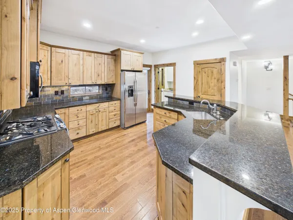 a kitchen with stainless steel appliances a stove top oven a sink a refrigerator white cabinets and wooden floor