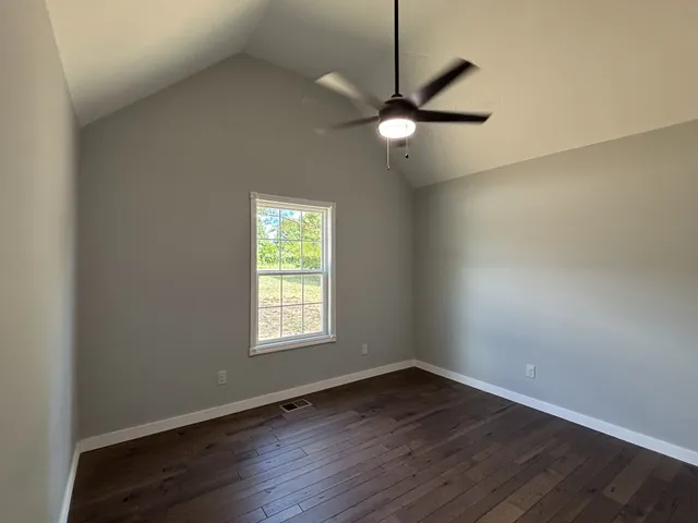 an empty room with wooden floor fan and windows